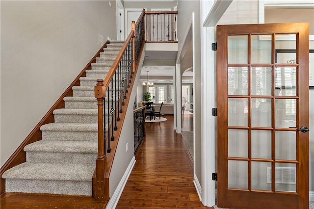 staircase with french doors, a towering ceiling, wood finished floors, baseboards, and a chandelier