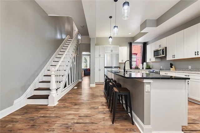 308 Jacksonia St, Central North Side, PA 15212 - kitchen with wood finished floors, an island with sink, a kitchen breakfast bar, white cabinetry, and stainless steel appliances