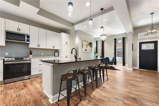 308 Jacksonia St, Central North Side, PA 15212 - kitchen with baseboards, a kitchen breakfast bar, white cabinetry, light wood-style flooring, and stainless steel appliances