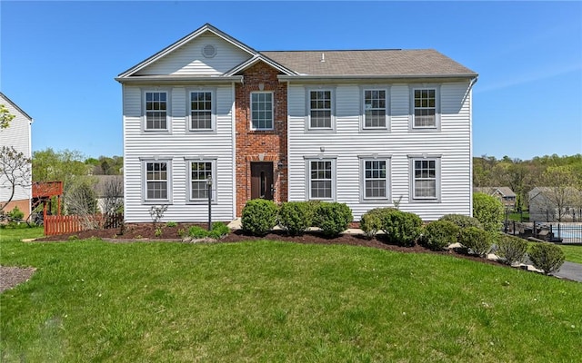 colonial-style house with brick siding, fence, a shingled roof, and a front yard