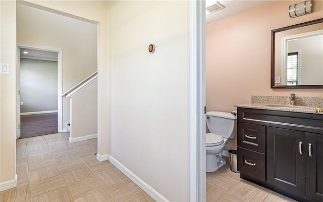 bathroom with baseboards, vanity, toilet, and visible vents