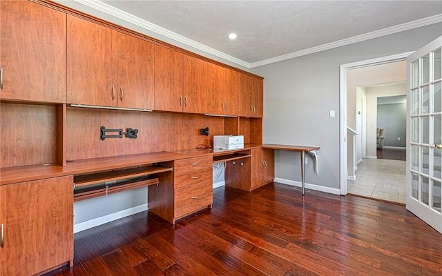 unfurnished office featuring crown molding, baseboards, dark wood finished floors, and built in study area