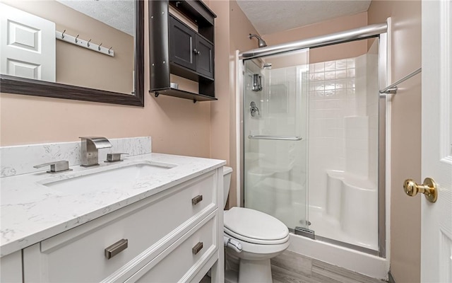 full bathroom featuring vanity, wood finished floors, toilet, a textured ceiling, and a shower stall