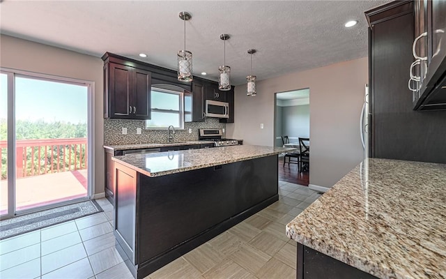 kitchen with a sink, stove, stainless steel microwave, tasteful backsplash, and a kitchen island