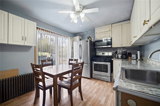 206 7th St, Oakmont, PA 15139 - kitchen featuring appliances with stainless steel finishes, radiator, a sink, ceiling fan, and light wood-style flooring