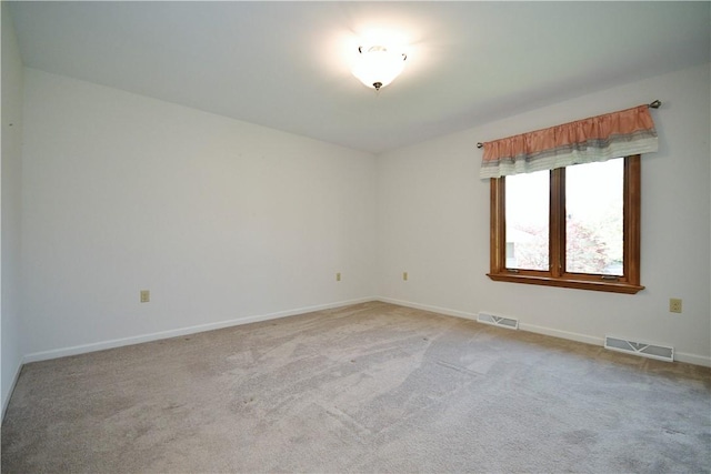 spare room featuring light colored carpet, baseboards, and visible vents