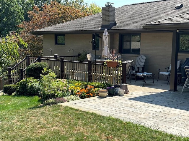 back of house featuring a lawn, a chimney, a shingled roof, and a patio area