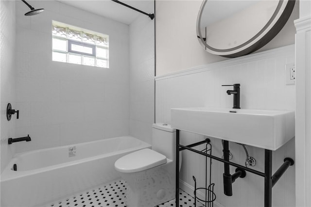 full bath with toilet, shower / washtub combination, wainscoting, and a sink