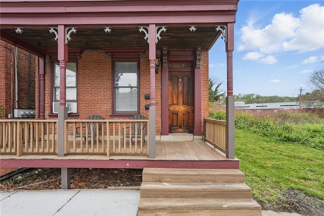 view of exterior entry with a porch and brick siding