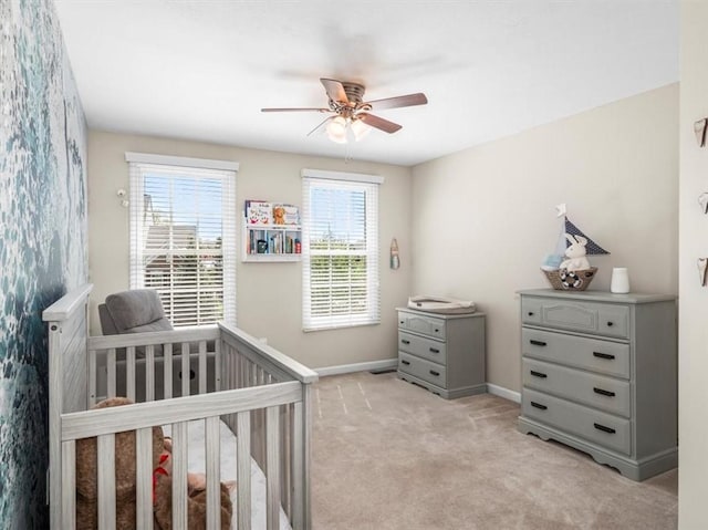 bedroom featuring baseboards, a ceiling fan, a crib, and light carpet