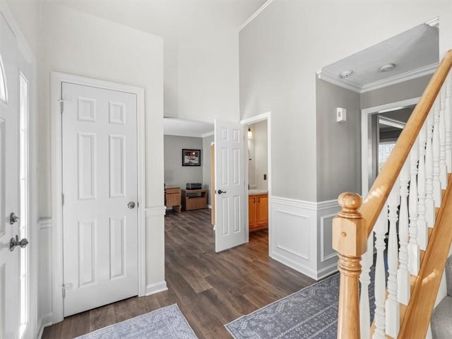 entrance foyer with ornamental molding, dark wood finished floors, a wainscoted wall, and stairway