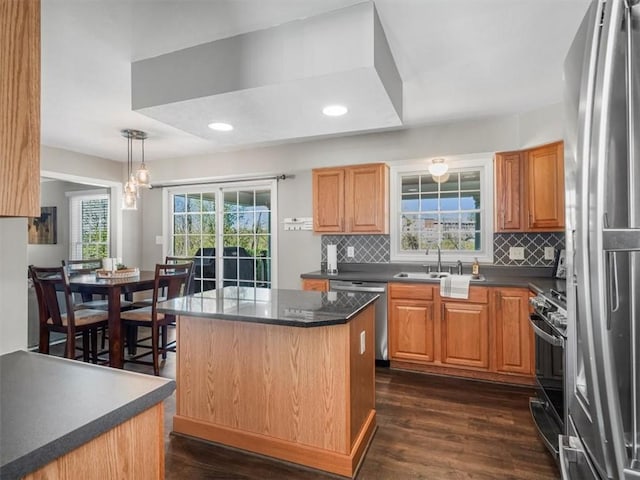 kitchen with dark countertops, a sink, stainless steel appliances, backsplash, and dark wood-style floors