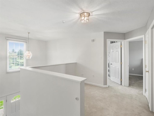 hallway featuring light colored carpet, baseboards, and an upstairs landing