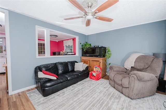 living area featuring baseboards, a ceiling fan, crown molding, and wood finished floors