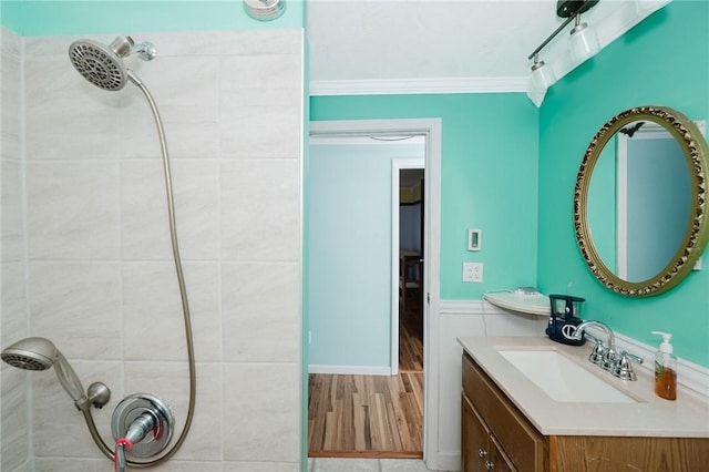 bathroom featuring crown molding, a tile shower, a wainscoted wall, and vanity