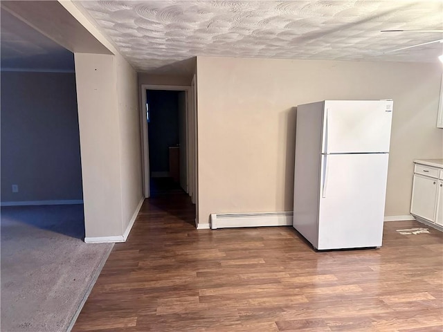 interior space with wood finished floors, freestanding refrigerator, a baseboard radiator, and white cabinets