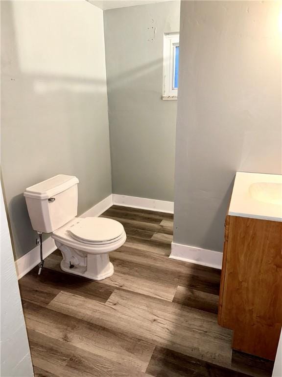 half bath with toilet, baseboards, wood finished floors, and vanity