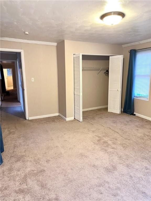 unfurnished bedroom featuring crown molding, baseboards, carpet, and a closet