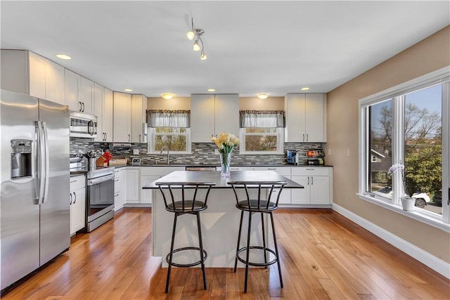 kitchen with dark countertops, appliances with stainless steel finishes, a breakfast bar, and backsplash