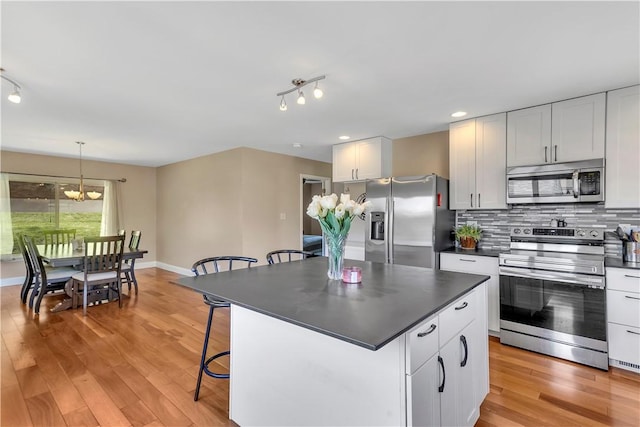 kitchen featuring a kitchen breakfast bar, backsplash, dark countertops, an inviting chandelier, and stainless steel appliances