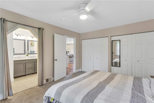 bedroom featuring visible vents, two closets, baseboards, light colored carpet, and connected bathroom