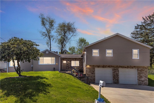 split level home featuring a garage, concrete driveway, and a lawn