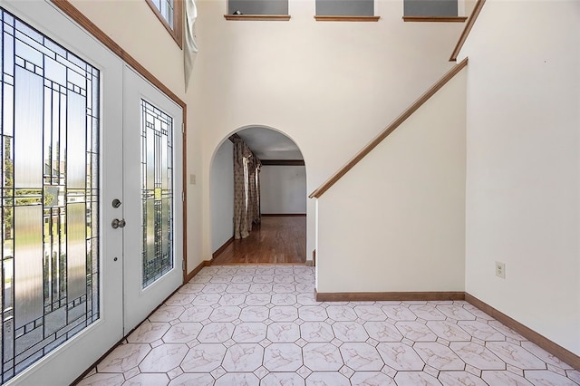 foyer featuring arched walkways, baseboards, and light floors