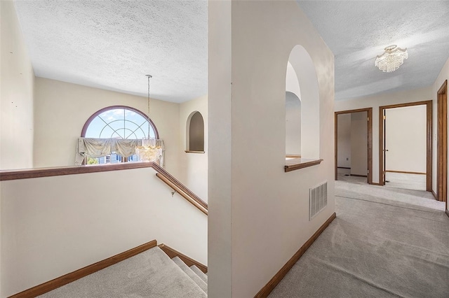 hall featuring baseboards, carpet, a textured ceiling, and visible vents
