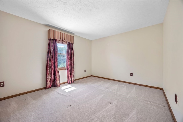 spare room featuring light colored carpet, a textured ceiling, and baseboards