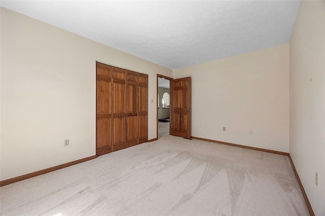 unfurnished bedroom with a closet, a textured ceiling, baseboards, and light carpet