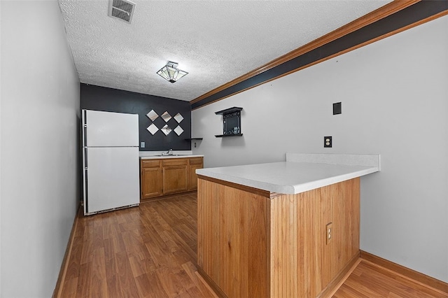 kitchen with a sink, freestanding refrigerator, a peninsula, dark wood-type flooring, and visible vents