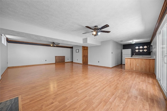unfurnished living room featuring light wood-type flooring, a textured ceiling, ceiling fan, and baseboards