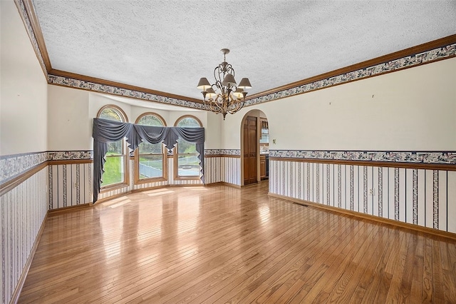 spare room featuring hardwood / wood-style flooring, a wainscoted wall, ornamental molding, and arched walkways
