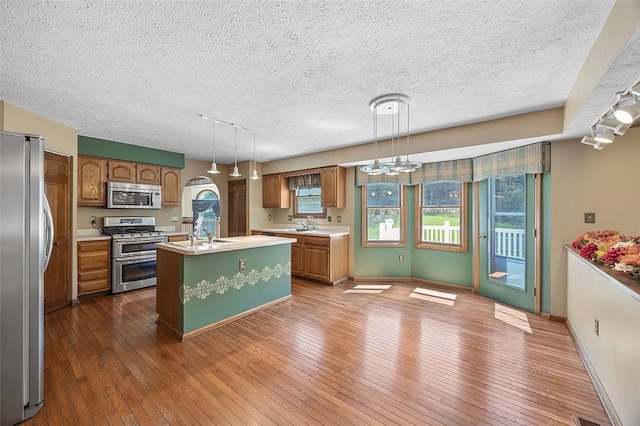 kitchen featuring dark wood-style flooring, a kitchen island with sink, light countertops, a textured ceiling, and stainless steel appliances