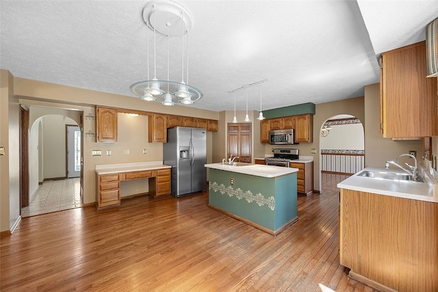 kitchen with a sink, appliances with stainless steel finishes, a center island with sink, and arched walkways