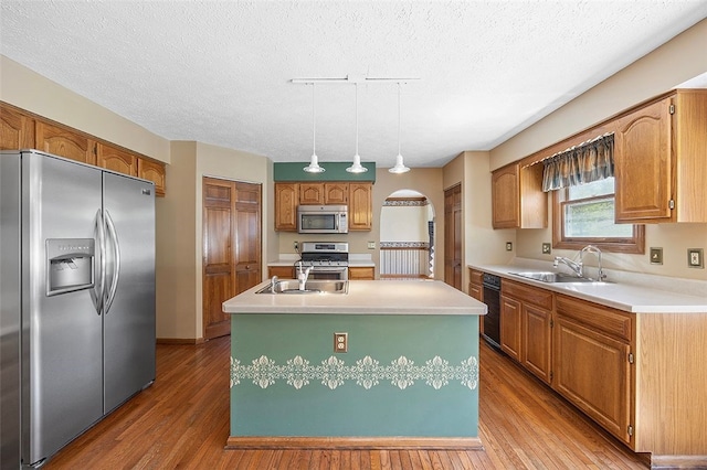 kitchen with appliances with stainless steel finishes, a sink, light countertops, an island with sink, and wood finished floors