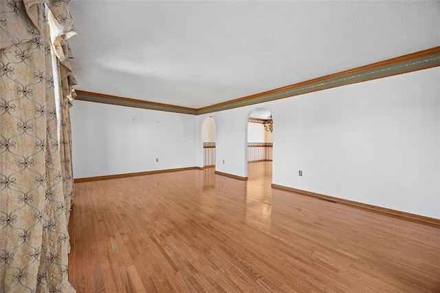 empty room featuring a textured ceiling, crown molding, arched walkways, baseboards, and hardwood / wood-style floors