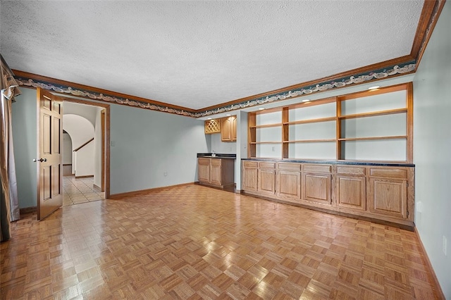 unfurnished living room featuring crown molding, baseboards, arched walkways, and a textured ceiling