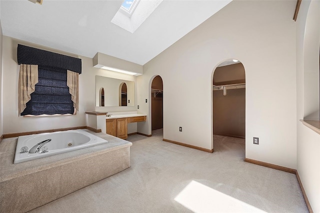 full bath featuring a jetted tub, a walk in closet, a skylight, vanity, and high vaulted ceiling