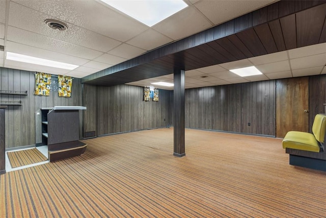 finished basement with visible vents, baseboards, wooden walls, a paneled ceiling, and carpet