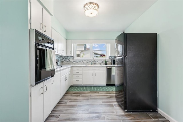 kitchen with tasteful backsplash, a sink, light countertops, white cabinets, and black appliances