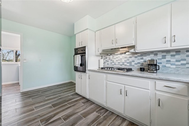 kitchen featuring oven, light countertops, under cabinet range hood, tasteful backsplash, and stainless steel gas stovetop