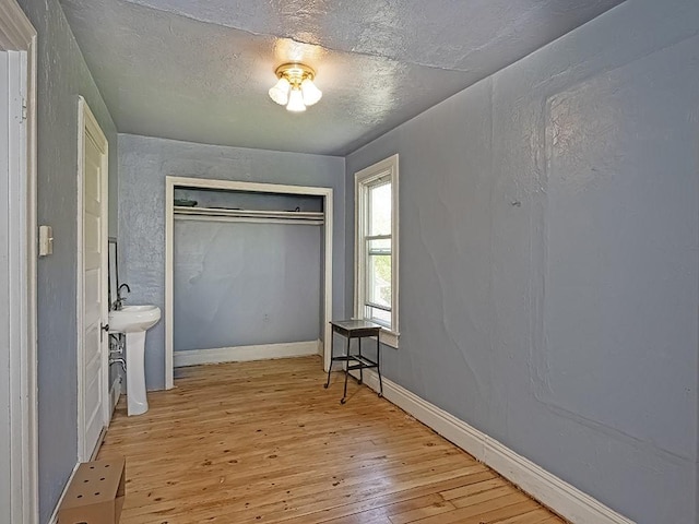 bedroom featuring a closet, hardwood / wood-style floors, baseboards, a textured ceiling, and a sink