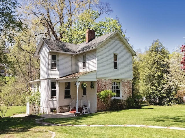 view of front of house with roof with shingles, brick siding, a front yard, a chimney, and a patio area