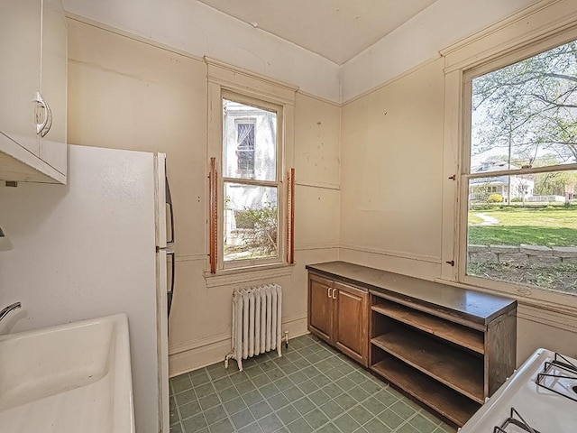 kitchen with freestanding refrigerator, open shelves, brown cabinetry, and radiator