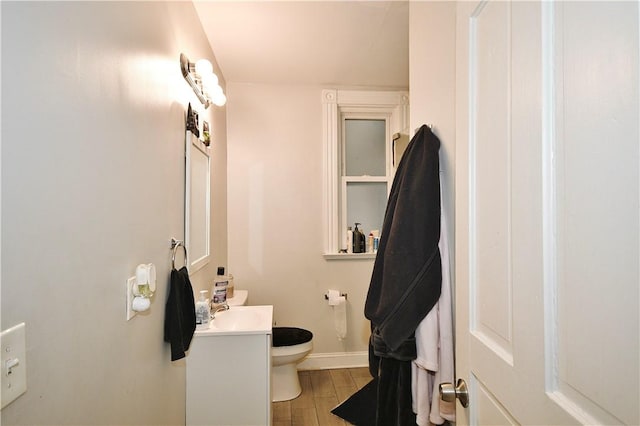 half bath featuring baseboards, vanity, toilet, and wood finished floors