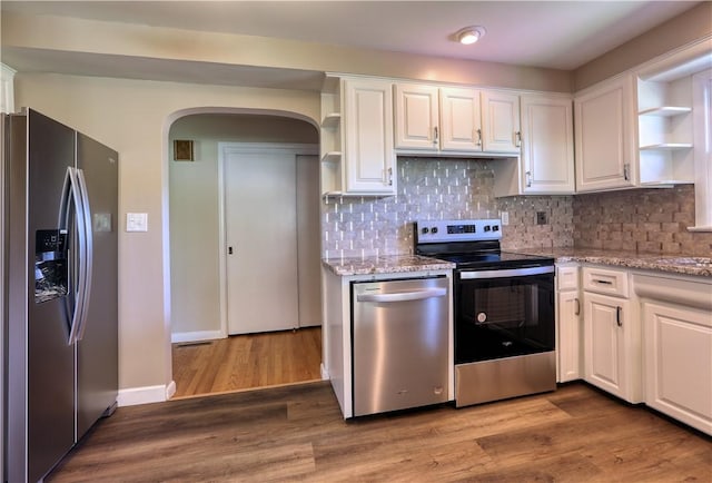 kitchen featuring appliances with stainless steel finishes, arched walkways, open shelves, light stone counters, and white cabinets