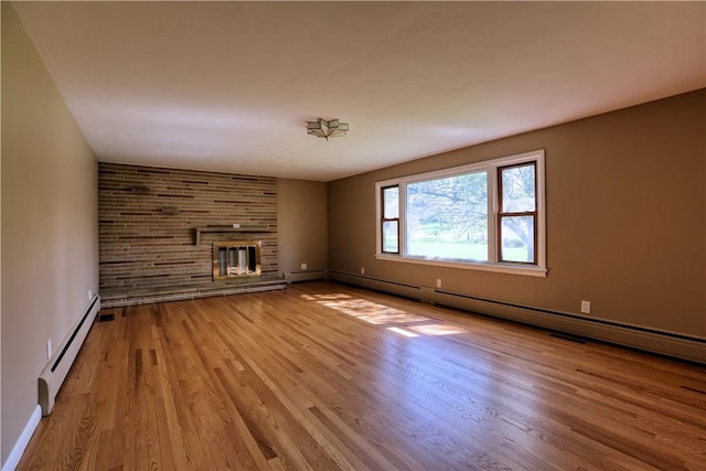 unfurnished living room featuring baseboards, a baseboard radiator, a brick fireplace, and wood finished floors