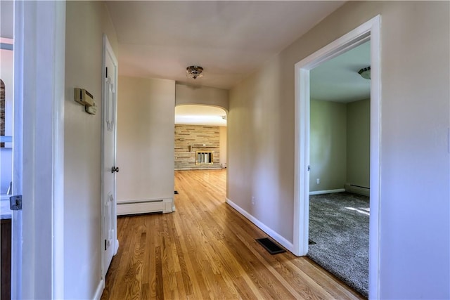 corridor featuring arched walkways, baseboard heating, wood finished floors, and visible vents