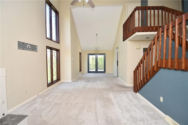 carpeted entrance foyer with baseboards, a ceiling fan, high vaulted ceiling, and stairway